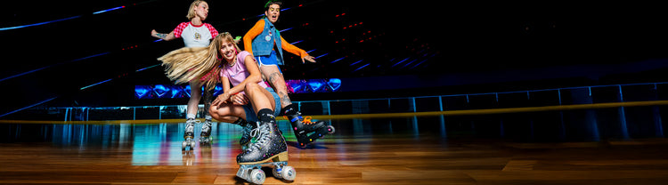Three people roller skating on a wooden floor with a dark background